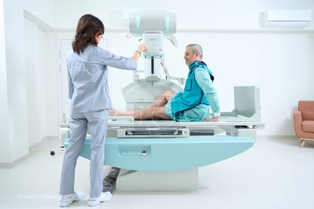 Foto de Radióloga mujer tomando rayos X de hombre en el hospital. Hospital moderno con equipos tecnológicamente avanzados - Imagen libre de derechos