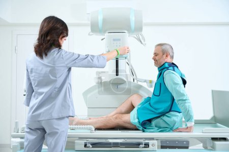 Téléchargez les photos : Médecin féminin préparant des appareils de radiographie pour la fabrication du roentgénogramme pour le patient. Un homme fait une radiographie du genou - en image libre de droit