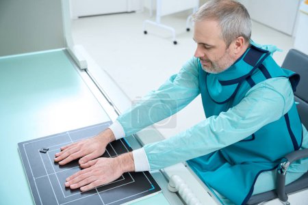 Téléchargez les photos : Homme adulte faisant des rayons X de ses deux mains sur l'équipement moderne dans la clinique - en image libre de droit