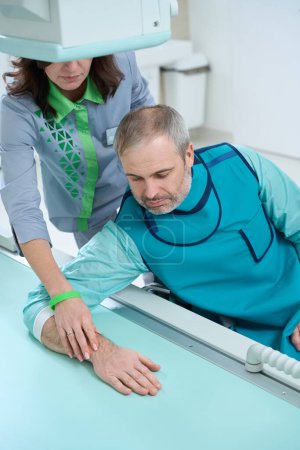 Foto de Médico femenino ayudando al paciente masculino durante la toma de rayos X en equipos modernos en la clínica - Imagen libre de derechos
