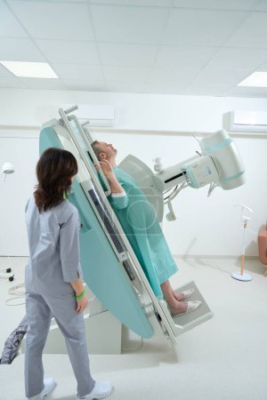Foto de Radiólogo profesional que ayuda a un paciente con la máquina de rayos X en una clínica - Imagen libre de derechos