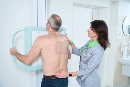 Photo for Female doctor standing near the male patient during chest X-Ray procedure in clinic - Royalty Free Image