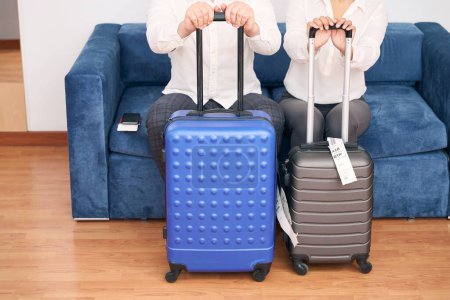 Téléchargez les photos : Photo recadrée de couple de touristes avec valises trolley assis sur un canapé confortable - en image libre de droit