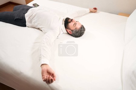 Foto de Sonriendo contento joven caballero acostado solo en la cama en su habitación de hotel - Imagen libre de derechos