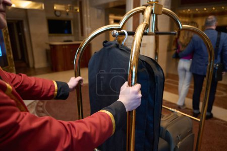 Téléchargez les photos : Un couple voyageur se promène dans le foyer d'un hôtel de luxe, suivi d'un porteur avec bagage - en image libre de droit