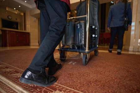 Foto de Huésped de un hotel de lujo pasea por el vestíbulo, seguido por el personal con equipaje - Imagen libre de derechos