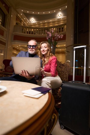 Foto de Hombre con gafas y buena mujer están buscando algo en el ordenador portátil, junto a ellos en la mesa hay pasaportes y billetes - Imagen libre de derechos