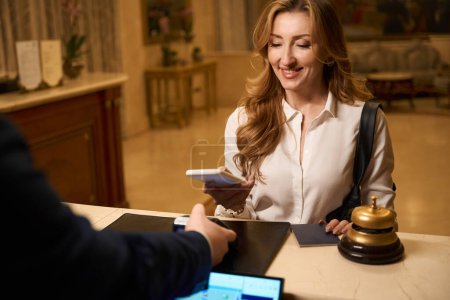 Foto de Viajero sonriente pasa el check-in en la recepción en el hotel, la recepcionista en su lugar de trabajo en el mostrador - Imagen libre de derechos