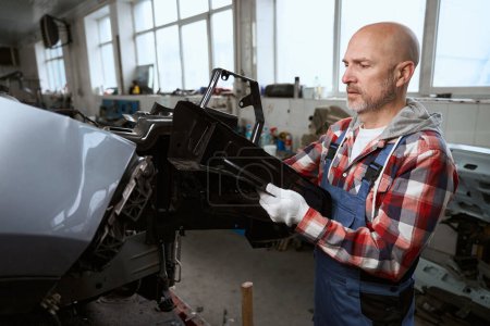 Photo for Man in a car repair shop disassembles a broken car for parts, a man in a plaid shirt - Royalty Free Image