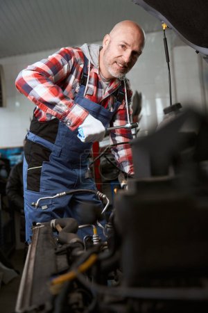 Foto de Hombre guapo en una camisa a cuadros está reparando un coche, el maestro utiliza una herramienta especial - Imagen libre de derechos