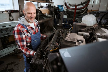 Téléchargez les photos : Travailleur d'âge moyen expérimenté fait des réparations de voiture, un homme en vêtements de travail - en image libre de droit