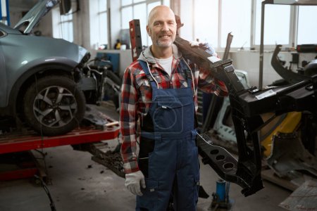 Photo for Strong master holds a part of the car body on his shoulder, a man in work overalls - Royalty Free Image