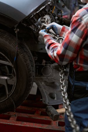 Foto de Hombre con guantes protectores sujeta un mosquetón con una cadena a la carrocería del coche - Imagen libre de derechos