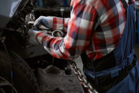 Photo for Worker in a car repair shop attaches a carabiner with a chain to the car body - Royalty Free Image