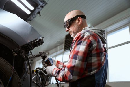 Photo for Specialist in protective glasses works as a spotter during a car repair, a man in work clothes - Royalty Free Image