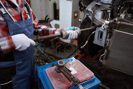 Téléchargez les photos : Spotter dans les mains d'un mécanicien automobile pendant les travaux de réparation dans un atelier automobile, un homme en vêtements de travail - en image libre de droit