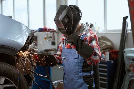 Foto de Soldador en overoles de trabajo trabaja en un taller de coches, sus guantes de protección hechos de material refractario - Imagen libre de derechos