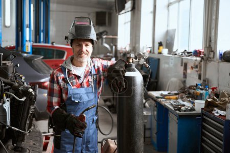 Repairman specialist stands in a workshop with a welding machine, a man leaned on a gas cylinder