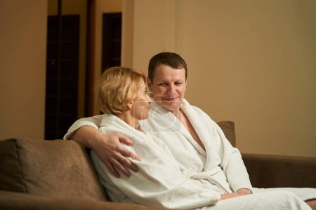 Photo for Spouses, embracing, sit on a soft sofa in a hotel room, they communicate nicely - Royalty Free Image