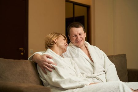 Photo for Couple are comfortably located in the recreation area of the hotel room, they communicate nicely, embracing - Royalty Free Image