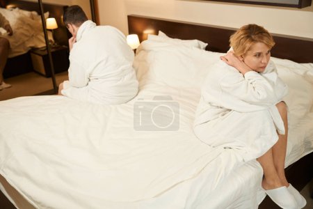 Foto de Quarreled hombre y mujer están sentados en lados opuestos de la cama, los cónyuges están en albornoces - Imagen libre de derechos