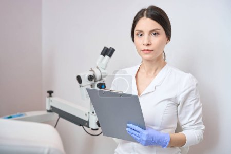 Téléchargez les photos : Gynécologue femelle est debout dans un bureau de clinique et tenant un bloc-notes dans ses mains - en image libre de droit