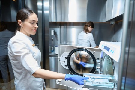 Photo for Female is holding the medical instruments on a special mesh and puting them into the autoclave for sterilization - Royalty Free Image