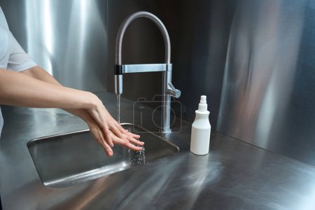Téléchargez les photos : Photo des mains féminines en cours de lavage avec de l'eau sous le robinet pour la stérilité dans une pièce spéciale de la clinique - en image libre de droit