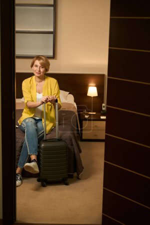 Foto de Viajando señora en jeans se sienta en el dormitorio de una habitación de hotel, la mujer condujo a un hotel moderno - Imagen libre de derechos