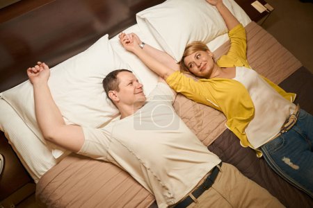 Foto de Alegre pareja casada descansando de la carretera en el dormitorio de una habitación de hotel, personas con ropa de viaje - Imagen libre de derechos