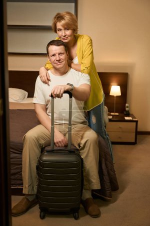 Téléchargez les photos : Voyageant couple marié enregistré dans un hôtel confortable moderne, ils se sont assis sur un grand lit dans une chambre d'hôtel - en image libre de droit