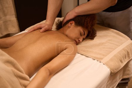 Photo for Woman is lying on sofa in room and getting massage of back from masseur - Royalty Free Image