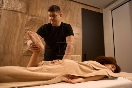 Photo for Osteopath is checking reflexes while flexing the leg of African American woman - Royalty Free Image