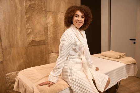 Photo for Happy woman in a bathrobe is smiling, waiting and siting on a couch in the spa - Royalty Free Image