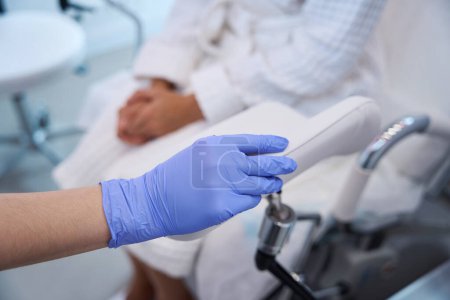 Téléchargez les photos : Femme main en gant médical jetable dans le cabinet de gynécologue clinique et brevet femelle en arrière-plan - en image libre de droit