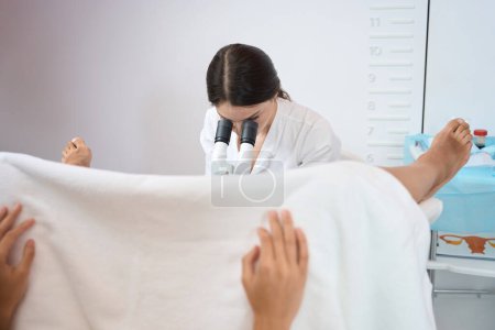 Téléchargez les photos : Gynécologue femelle est assis et fait un examen de l'utérus du patient à l'aide d'un microscope - en image libre de droit