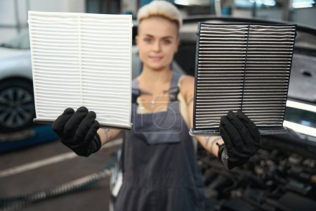 Téléchargez les photos : Vue rapprochée des employées mains dans les gants montrant les filtres à air cabine dans le service de réparation automobile - en image libre de droit