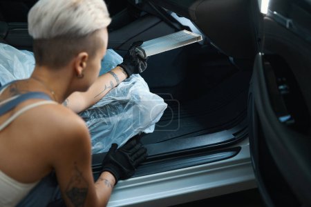 Téléchargez les photos : Vue arrière de la travailleuse blonde avec une coupe de cheveux élégante insérant des détails dans la voiture - en image libre de droit