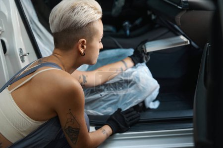 Foto de Vista recortada en diligente mecánico femenino en uniforme de trabajo que instala parte en auto dentro del coche - Imagen libre de derechos
