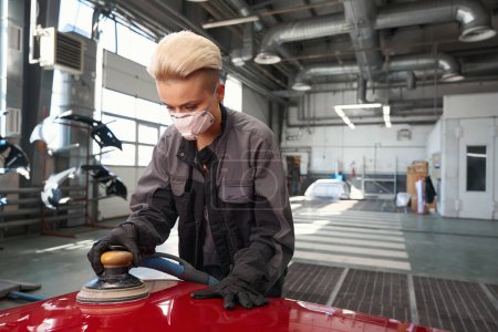 Photo for Female auto mechanic worker in protective mask and gloves polishing car by power buffer machine at renewing service station shop - Royalty Free Image