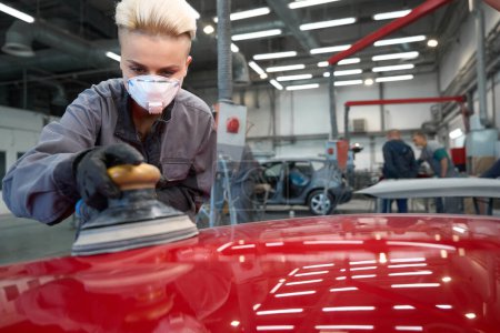 Photo for Photo of responsabile female employee with stylish haircut polishing car with auto mechanics on background - Royalty Free Image