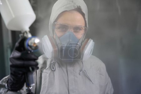 Photo for Close up view of professional woman worker in workwear looking and spraying paint at camera - Royalty Free Image