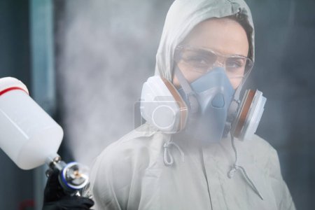 Téléchargez les photos : Portrait d'une employée diligente en respirateur et lunettes regardant et utilisant la pulvérisation à la caméra - en image libre de droit