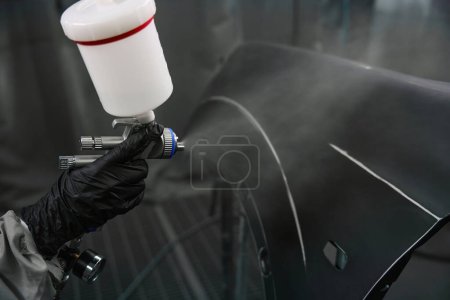 Close up view on hand of car technician in rubber glove dyeing car element using spray gun