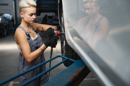 Foto de El mecánico del coche de la mujer desenrosca los pernos en una rueda del coche, equipo moderno se utiliza en un taller de reparación del coche - Imagen libre de derechos