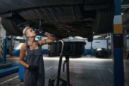 Foto de Empleado de un taller de reparación de automóviles trabaja con un coche criado en un ascensor especial, un profesional en guantes de protección - Imagen libre de derechos