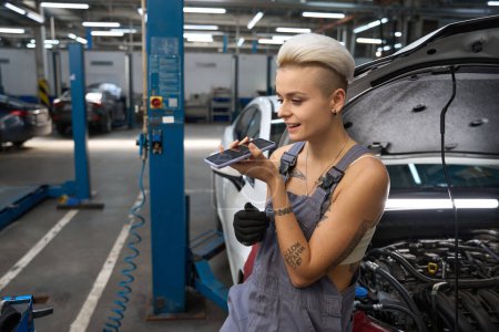 Photo for Employee of a car repair shop is standing among the cars, the craftswoman is talking on the phone - Royalty Free Image