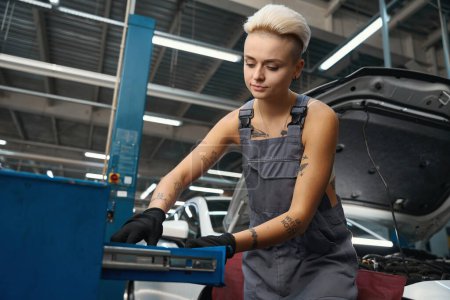 Téléchargez les photos : Femme réparateur automobile sur le lieu de travail près de la boîte de travail avec des outils, équipement moderne dans l'atelier - en image libre de droit