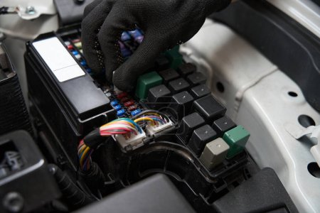 Autoreparator überprüft die Sicherung im elektrischen System des Autos, der Mann arbeitet in Schutzhandschuhen