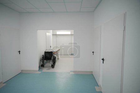 Téléchargez les photos : Lit postopératoire mobile et un fauteuil roulant sont situés dans un couloir d'hôpital lumineux spacieux - en image libre de droit